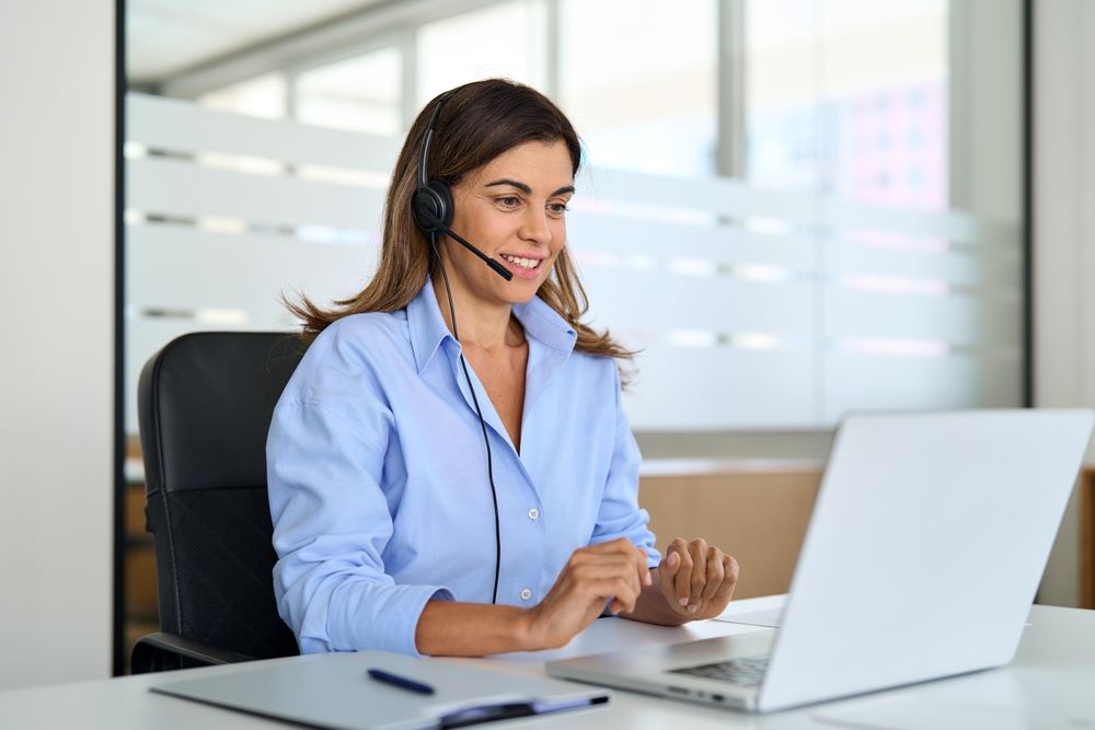 Une femme d'âge mûr opératrice d'assistance parlant à un client assis au bureau.